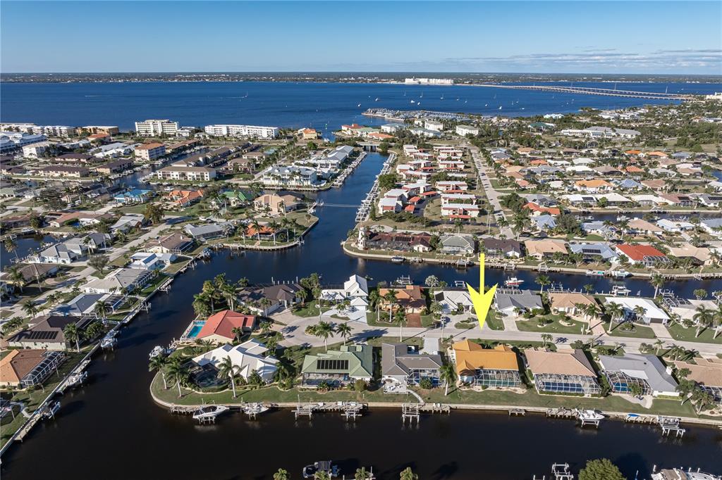 An aerial view shows a waterfront house with a yellow roof and pool cage — 1119 VIA FORMIA, PUNTA GORDA, FL