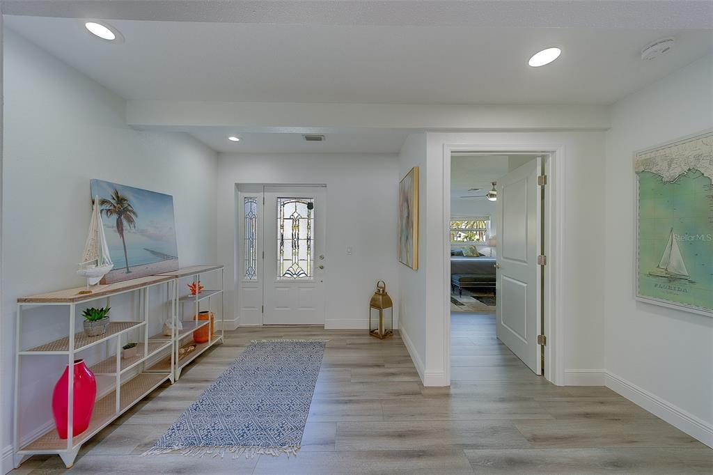 A bright entryway features light wood-look flooring, a white front door, and a console table — 2109 BAYSHORE DRIVE, BELLEAIR BEACH, FL