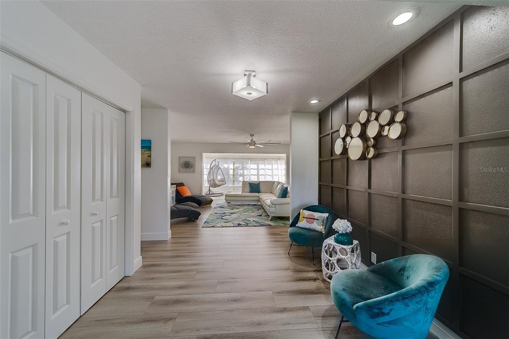 A hallway with wood-look flooring leads to a living room featuring a dark accent wall — 2109 BAYSHORE DRIVE, BELLEAIR BEACH, FL