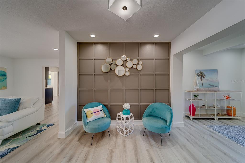 A living area features a paneled accent wall, two teal chairs, and light wood flooring — 2109 BAYSHORE DRIVE, BELLEAIR BEACH, FL