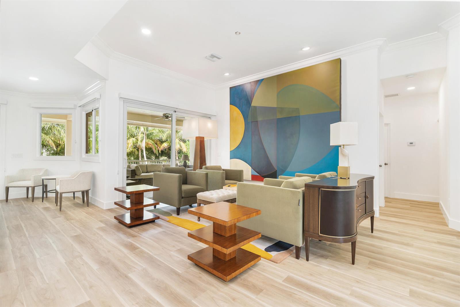 A living room features light wood flooring, green armchairs, tiered wooden tables, and large abstract art — 3317 Embassy Drive, West Palm Beach FL 33401, WEST PALM BEACH, FL