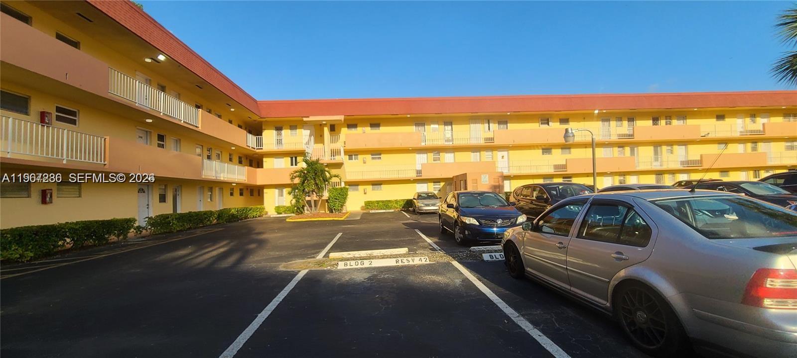 A multi-story yellow apartment building with a parking lot in the foreground — 1540 NE 191st St # 207, Miami FL 33179, MIAMI, FL