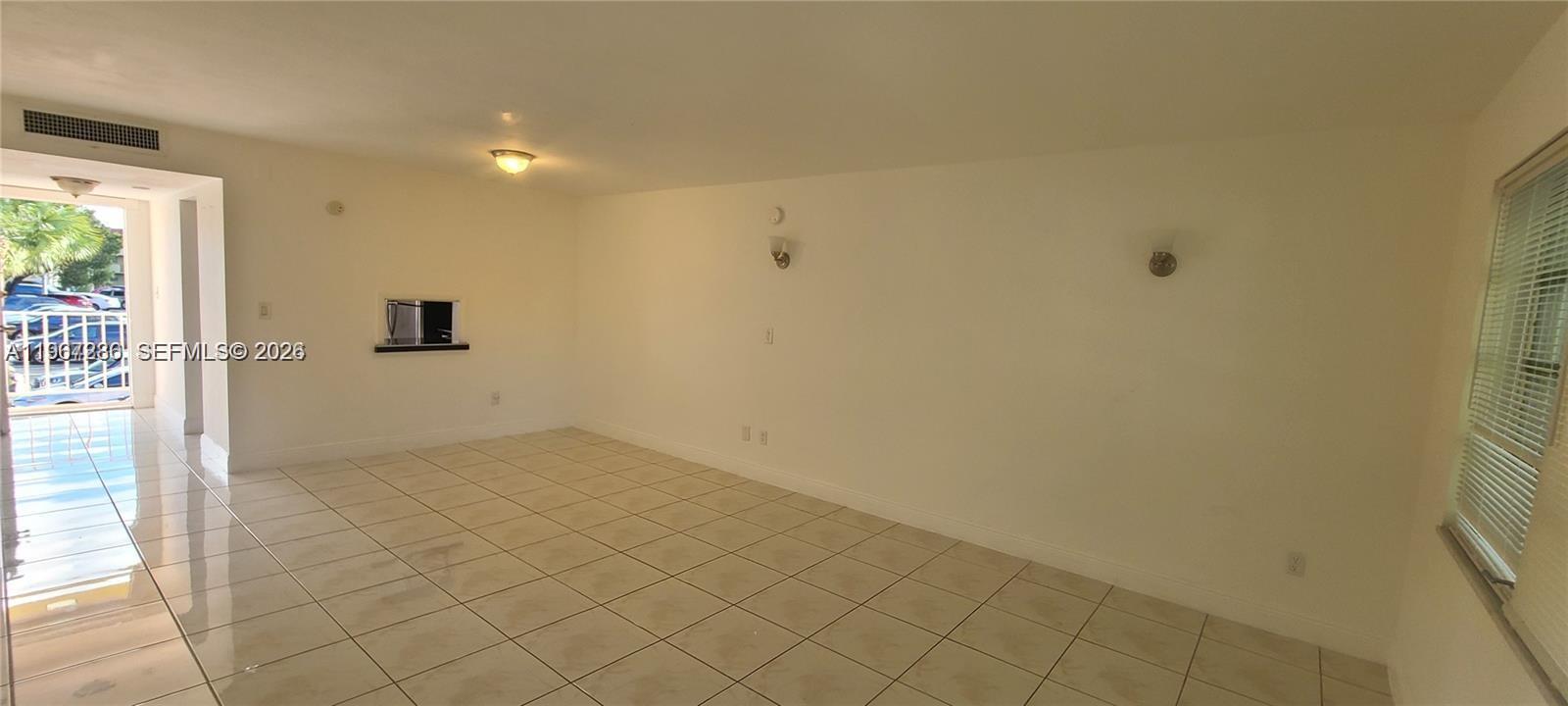 An empty room features light-colored tile flooring, white walls, and a sliding glass door — 1540 NE 191st St # 207, Miami FL 33179, MIAMI, FL