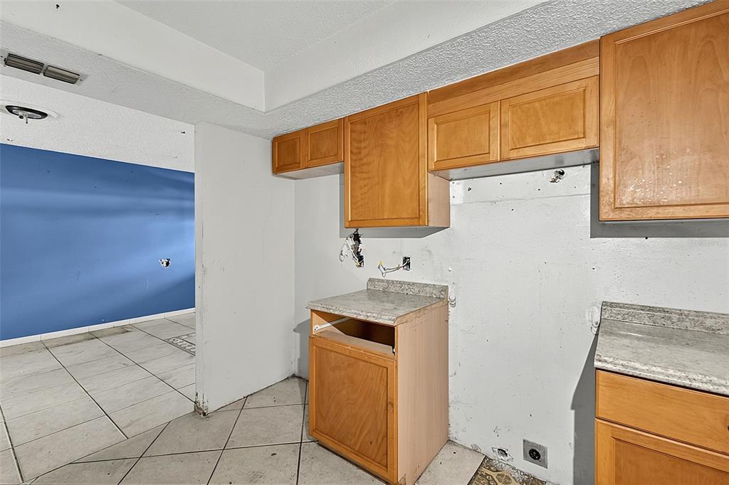 An unfinished kitchen features light wood cabinets, granite-style countertops, and white tile flooring — 4830 COCO PALM DRIVE, SEBRING, FL