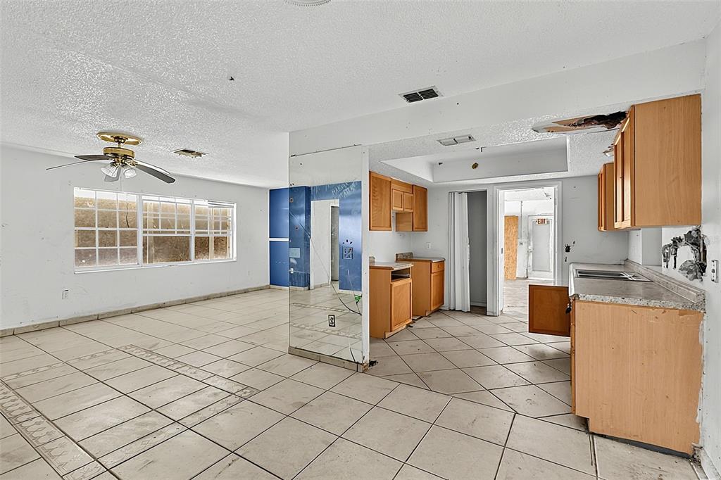 A room with blue walls, tiled floors, a ceiling fan, and a partial kitchen view — 4830 COCO PALM DRIVE, SEBRING, FL