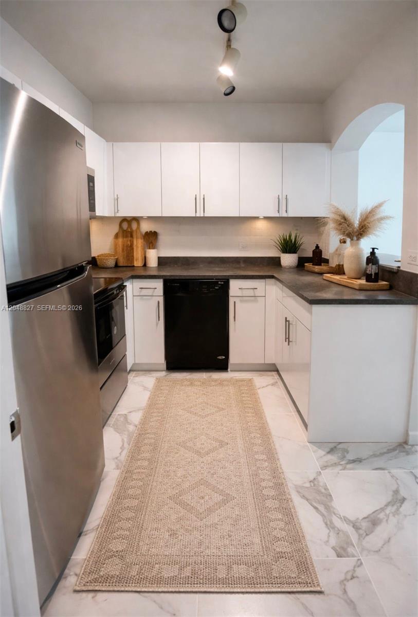 A kitchen features white cabinets, dark countertops, stainless steel appliances, and a patterned area rug — 9172 Collins Ave # 214, Surfside FL 33154, SURFSIDE, FL