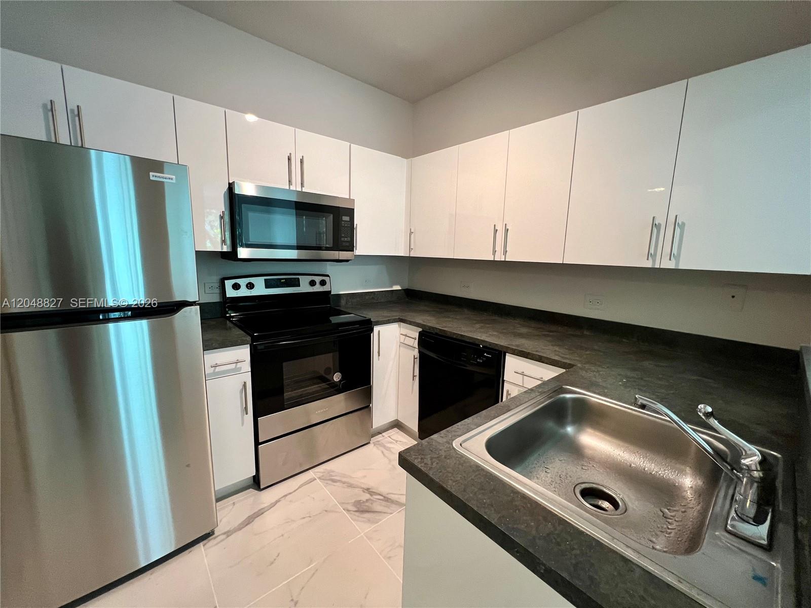 A modern kitchen features white cabinets, stainless steel appliances, and dark countertops — 9172 Collins Ave # 214, Surfside FL 33154, SURFSIDE, FL