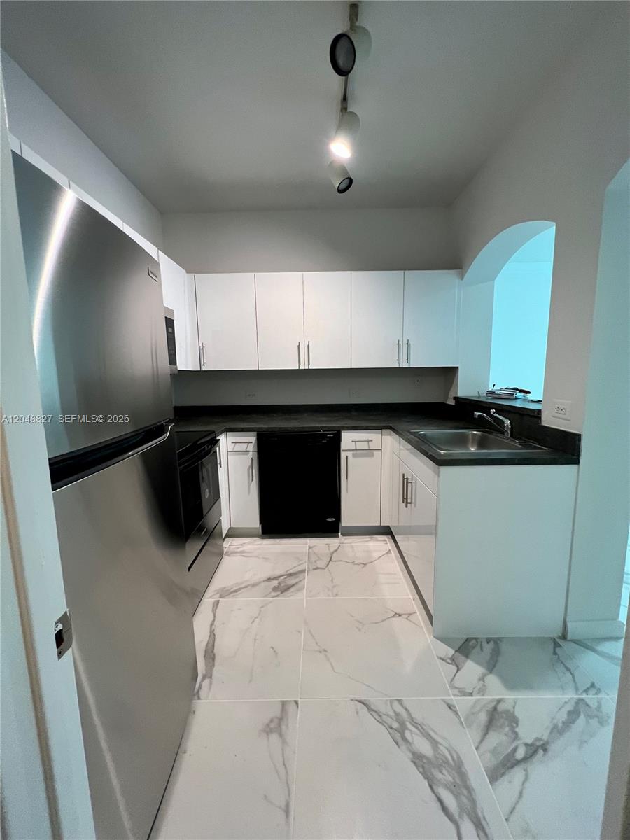 A galley kitchen features white cabinets, stainless steel appliances, dark countertops, and marble-look tile flooring — 9172 Collins Ave # 214, Surfside FL 33154, SURFSIDE, FL