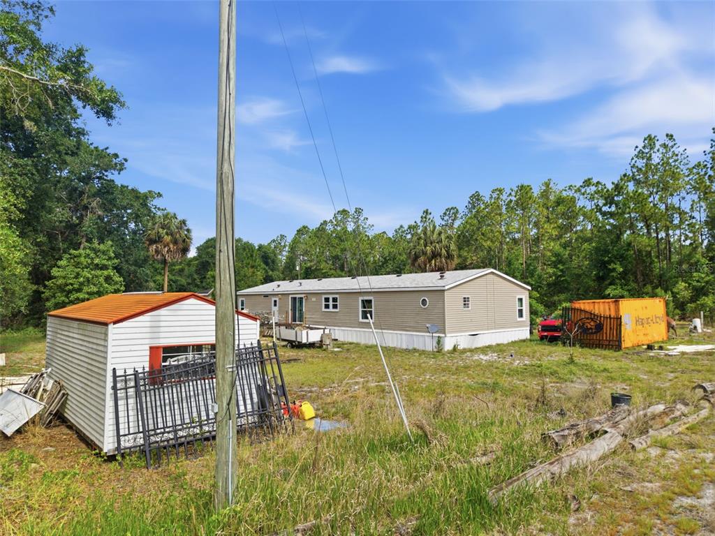 A mobile home sits on a grassy lot with a shed and shipping container nearby — 9780 MIDWAY ROAD, HAINES CITY, FL