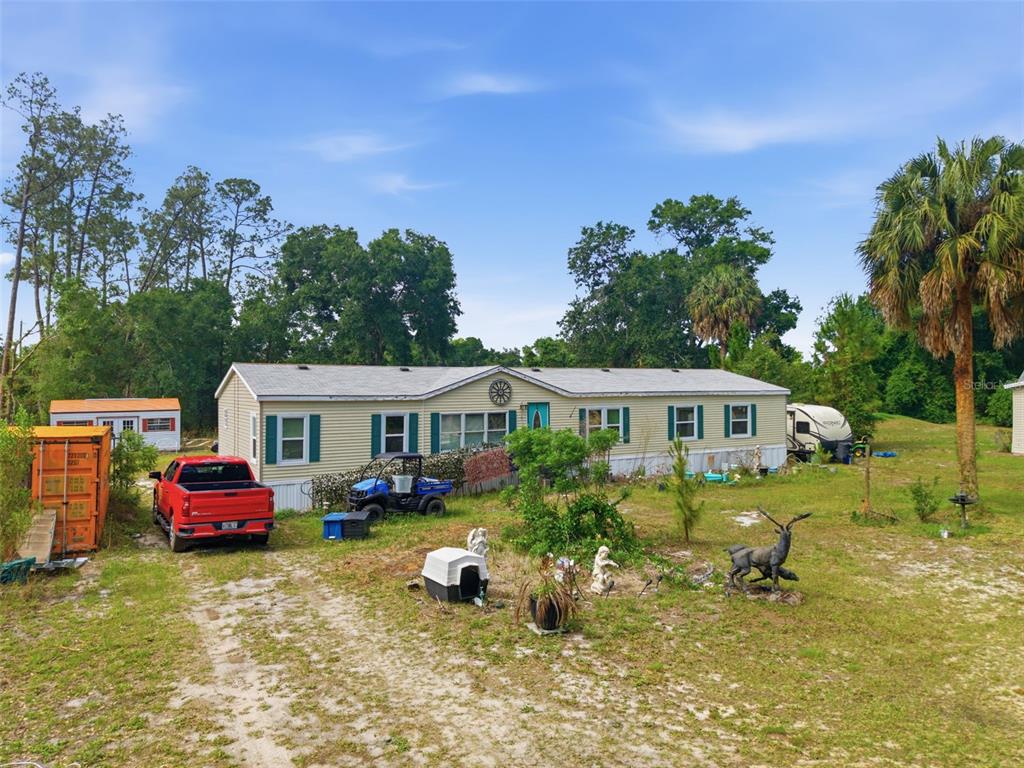 A single-story manufactured home with light siding sits on a large, grassy, rural lot — 9780 MIDWAY ROAD, HAINES CITY, FL