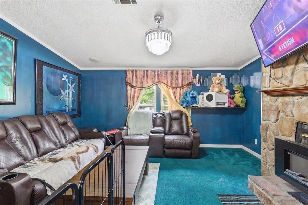 A living room features blue walls, teal carpeting, a stone fireplace, and brown leather furniture — 9780 MIDWAY ROAD, HAINES CITY, FL