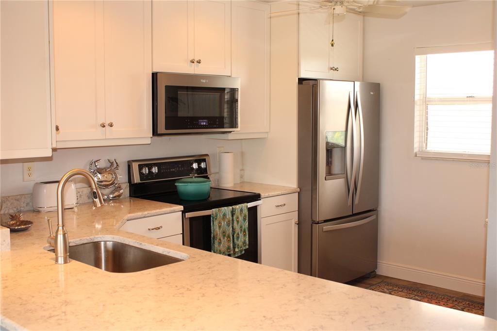 A kitchen features white cabinets, stainless steel appliances, and light-colored stone countertops — 4240 IRONWOOD CIRCLE UNIT 404, BRADENTON, FL