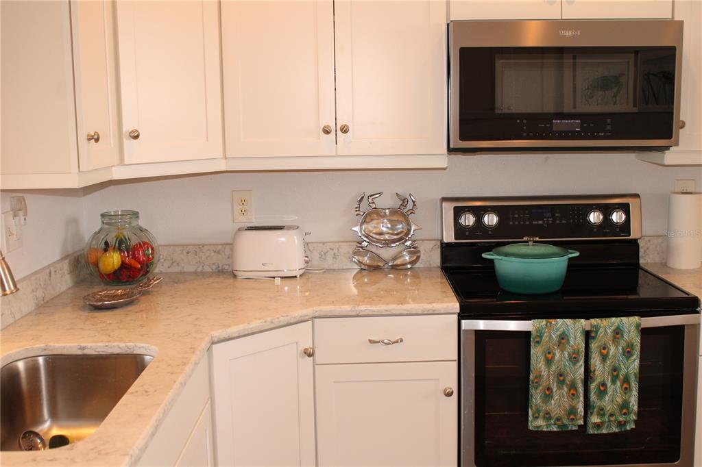 A kitchen features white cabinets, light countertops, a stainless steel microwave, and a black stove — 4240 IRONWOOD CIRCLE UNIT 404, BRADENTON, FL