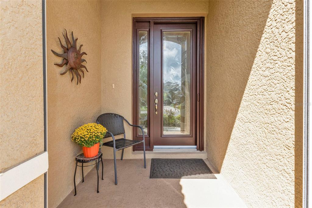 A covered entryway features a brown front door with glass panels, a chair, and decor — 13139 PRESERVE COURT, PORT CHARLOTTE, FL