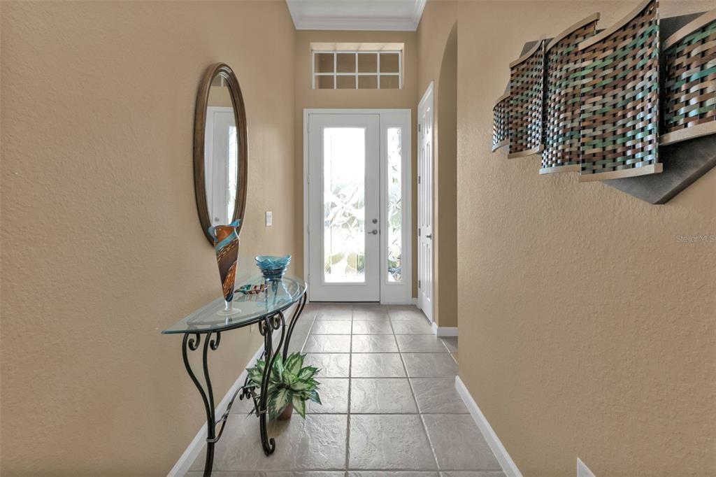 A tiled entryway features a glass console table, a wall mirror, and a decorative wall sculpture — 13139 PRESERVE COURT, PORT CHARLOTTE, FL