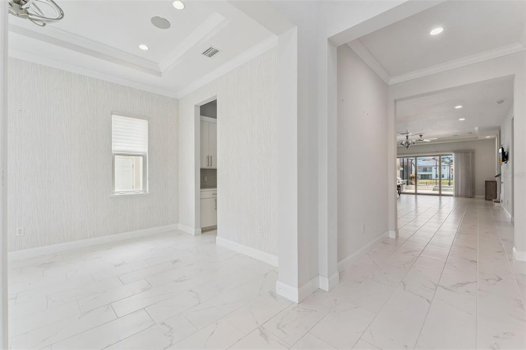 A bright room with white marble-look tile floors and textured wallpaper leads to a hallway — 10763 ROYAL CYPRESS WAY, ORLANDO, FL