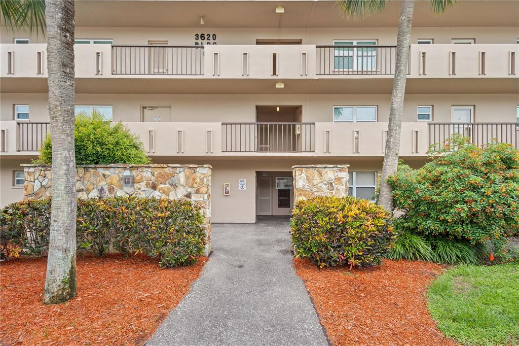 A multi-story apartment building exterior features a stone wall, landscaping, and a central walkway — 3620 IRONWOOD CIRCLE UNIT 302O, BRADENTON, FL