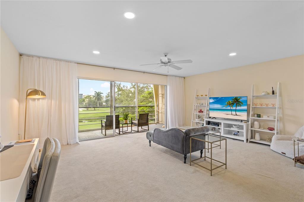 A living room with beige carpet, a grey sofa, a television, and a balcony view — 3620 IRONWOOD CIRCLE UNIT 302O, BRADENTON, FL