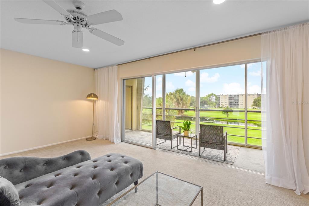 A living room with a tufted gray chaise, glass coffee table, and sliding glass balcony doors — 3620 IRONWOOD CIRCLE UNIT 302O, BRADENTON, FL