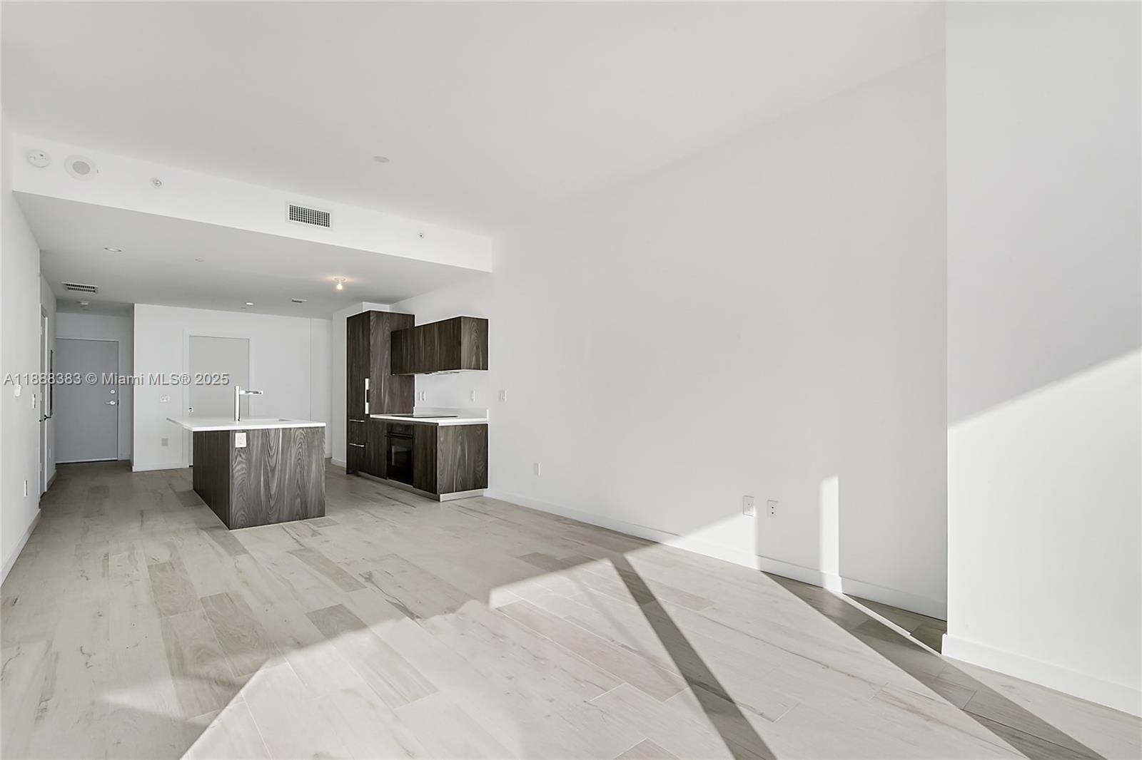 A modern kitchen with dark wood cabinetry and a central island sits in an open-plan room — 480 NE 31st St # 904, Miami FL 33137, MIAMI, FL