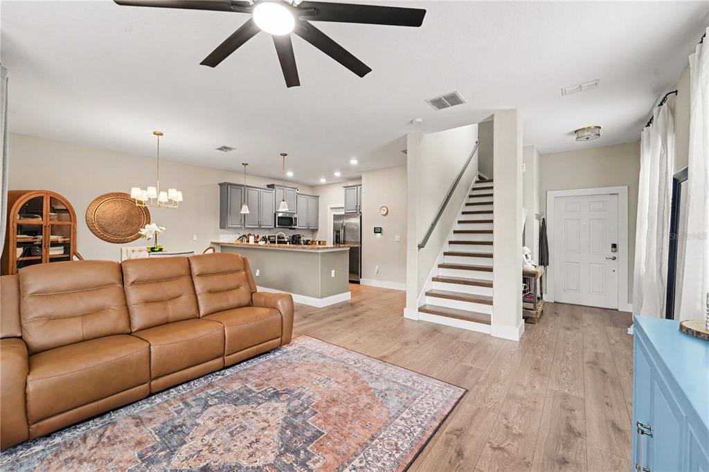 An open-concept living room features a brown leather sofa, wood flooring, and a staircase — 28425 PLEASANT BAY LOOP, WESLEY CHAPEL, FL
