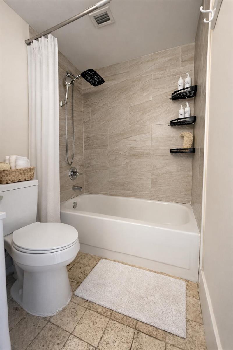 A bathroom features a white toilet, a bathtub with a shower head, and tiled walls — 2837 N Course Drive # 202, Pompano Beach FL 33069, POMPANO BEACH, FL