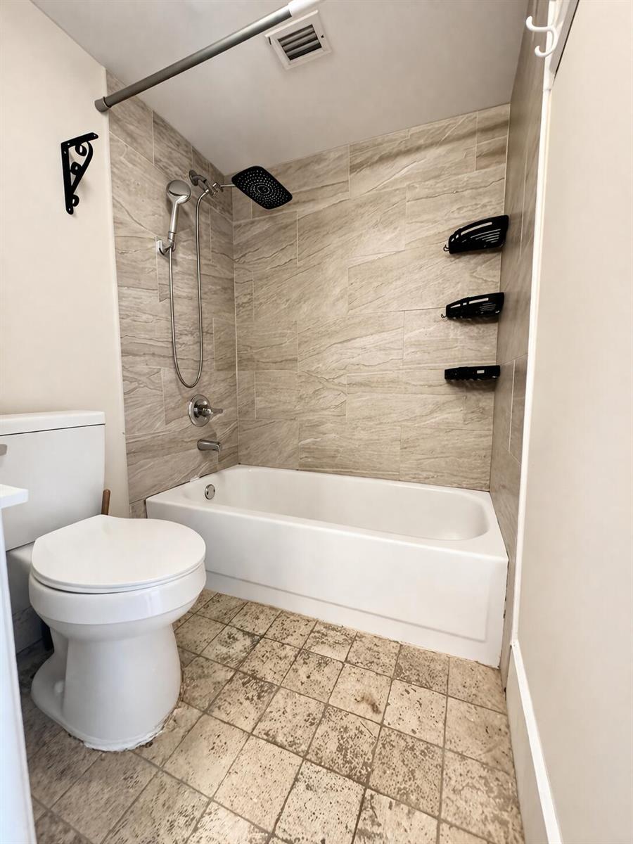 A bathroom features a white toilet, a bathtub with a showerhead, and beige tiled walls — 2837 N Course Drive # 202, Pompano Beach FL 33069, POMPANO BEACH, FL