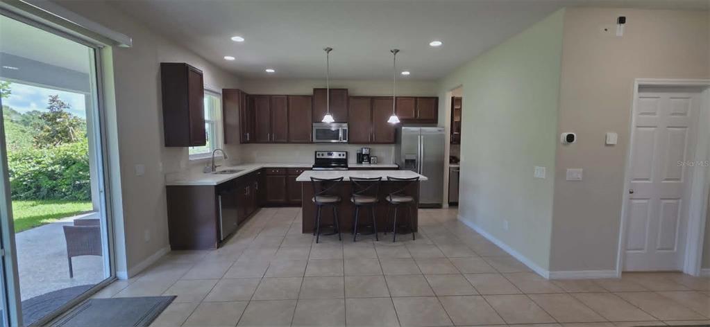 A kitchen features dark wood cabinets, stainless steel appliances, a center island, and tile flooring — 5177 DOVE TREE STREET, ORLANDO, FL
