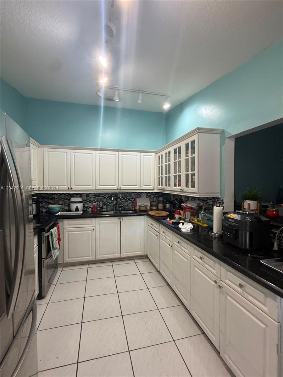 A kitchen features white cabinets, black countertops, a tiled backsplash, and light blue walls — 17401 SW 144th Ct, Miami FL 33177, MIAMI, FL