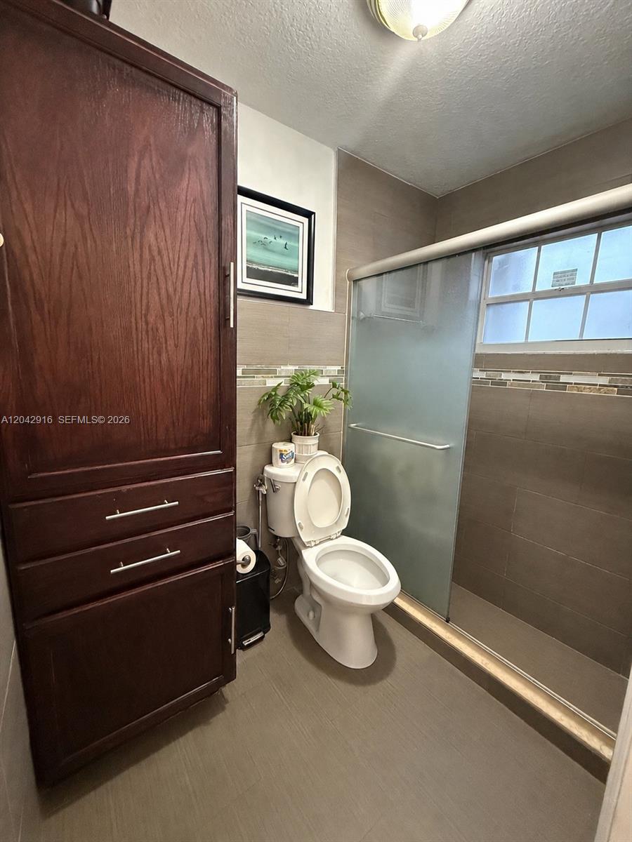 A bathroom features a tall wooden cabinet, a white toilet, and a tiled walk-in shower — 17401 SW 144th Ct, Miami FL 33177, MIAMI, FL