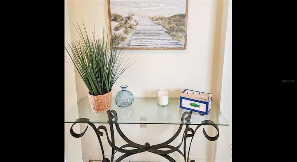 A glass-topped console table with a metal base sits against a wall with artwork — 1318 SIESTA BAYSIDE DRIVE UNIT C, SARASOTA, FL
