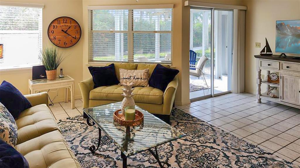 A living room features two light-colored sofas, a glass coffee table, and a large wall clock — 1318 SIESTA BAYSIDE DRIVE UNIT C, SARASOTA, FL