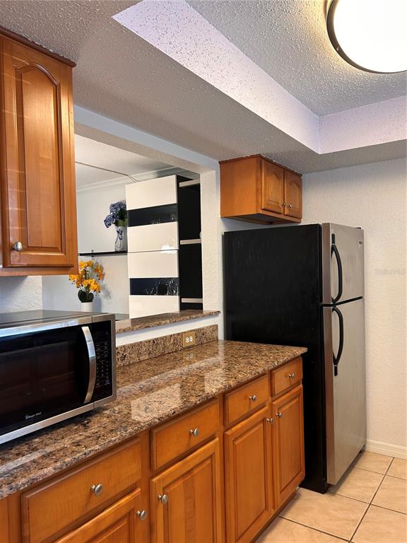 A kitchen features wood cabinets, granite countertops, a microwave, and a stainless steel refrigerator — 972 LA COSTA CIRCLE UNIT 3, SARASOTA, FL