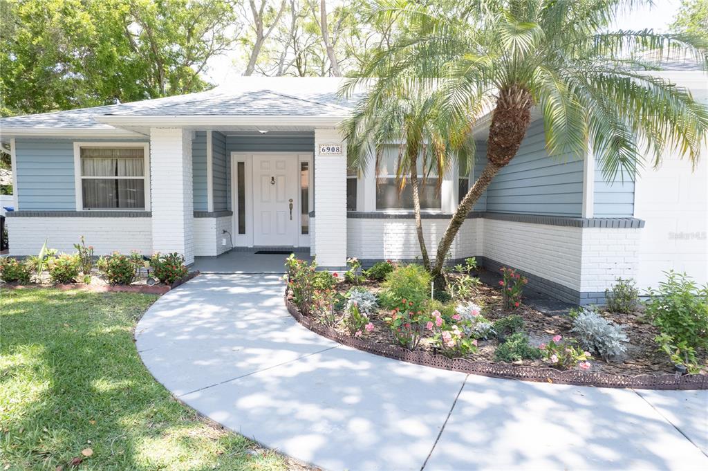 A single-story house features blue siding, white brick accents, a palm tree, and a walkway — 6908 ARBOR OAKS CIRCLE, BRADENTON, FL