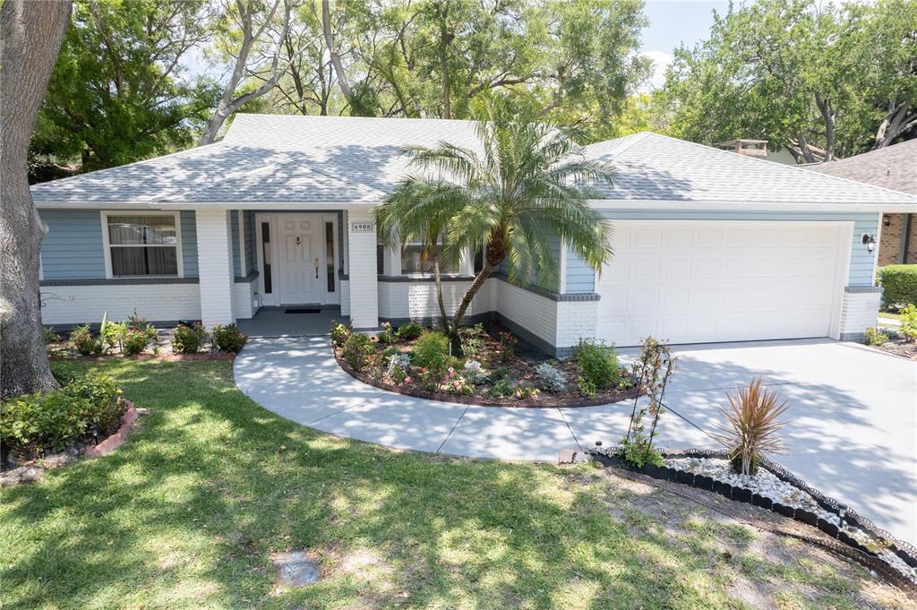 A single-story house with blue siding, white brick accents, a palm tree, and a concrete driveway — 6908 ARBOR OAKS CIRCLE, BRADENTON, FL