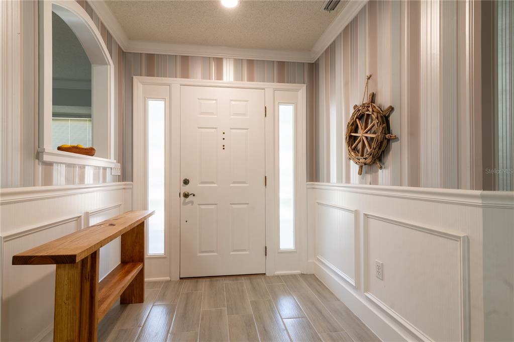 A foyer features a white front door, wood-look tile floors, wainscoting, and striped wallpaper — 6908 ARBOR OAKS CIRCLE, BRADENTON, FL