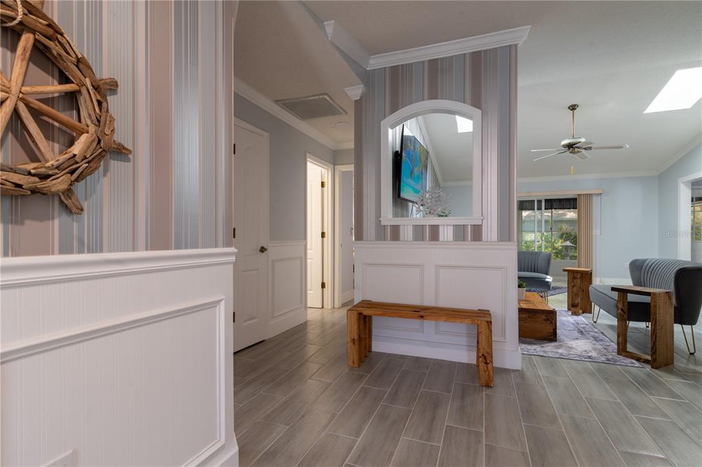 A hallway with wood-look tile flooring leads to a living area featuring a decorative bench — 6908 ARBOR OAKS CIRCLE, BRADENTON, FL