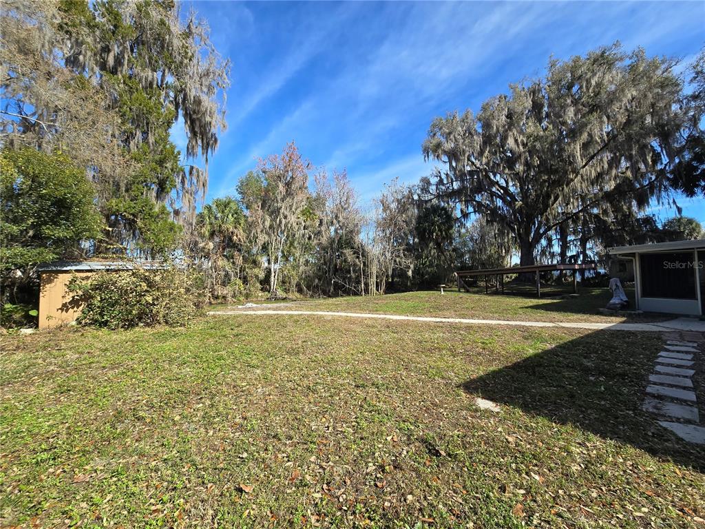 A grassy backyard features a small shed, a wooden deck, and large moss-covered trees — 2346 CR 401, LAKE PANASOFFKEE, FL
