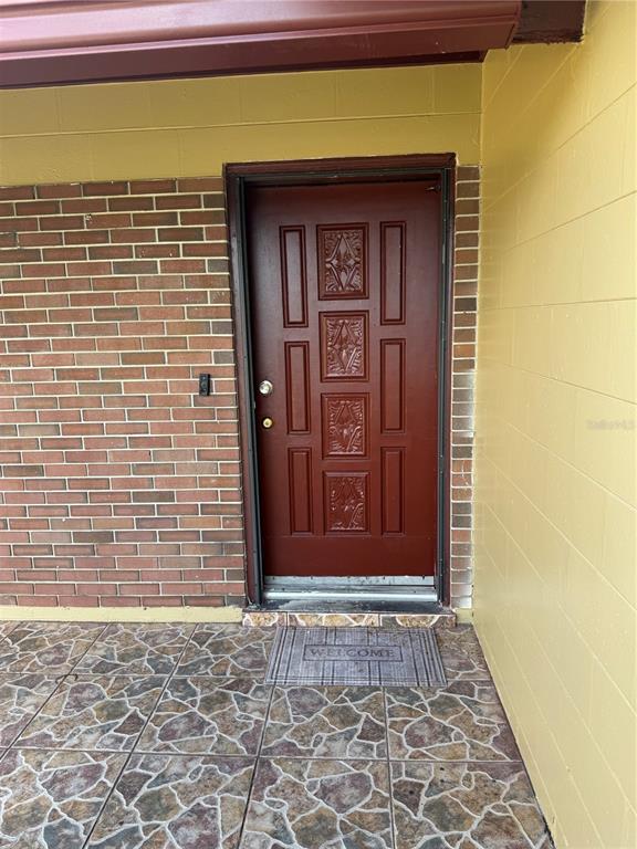 A red front door is set into a brick and yellow block wall above tiled flooring — 5816 VIKING ROAD, ORLANDO, FL