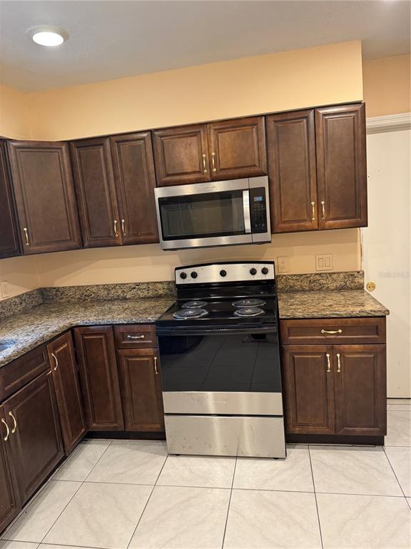 A kitchen features dark wood cabinets, granite countertops, and stainless steel appliances — 5816 VIKING ROAD, ORLANDO, FL