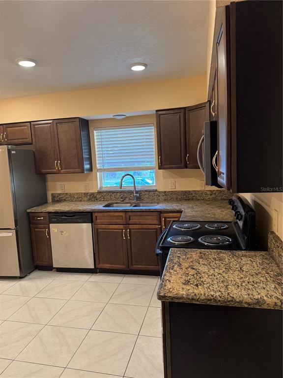 A kitchen features dark wood cabinets, granite countertops, stainless steel appliances, and light tile flooring — 5816 VIKING ROAD, ORLANDO, FL