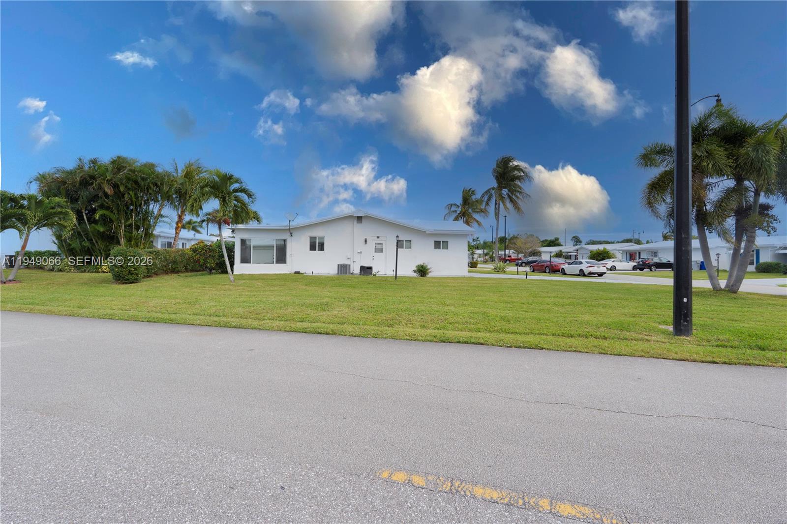 A white single-story house sits on a grassy lot with palm trees under a sky — 131 NW 31st Ct, Pompano Beach FL 33064, POMPANO BEACH, FL