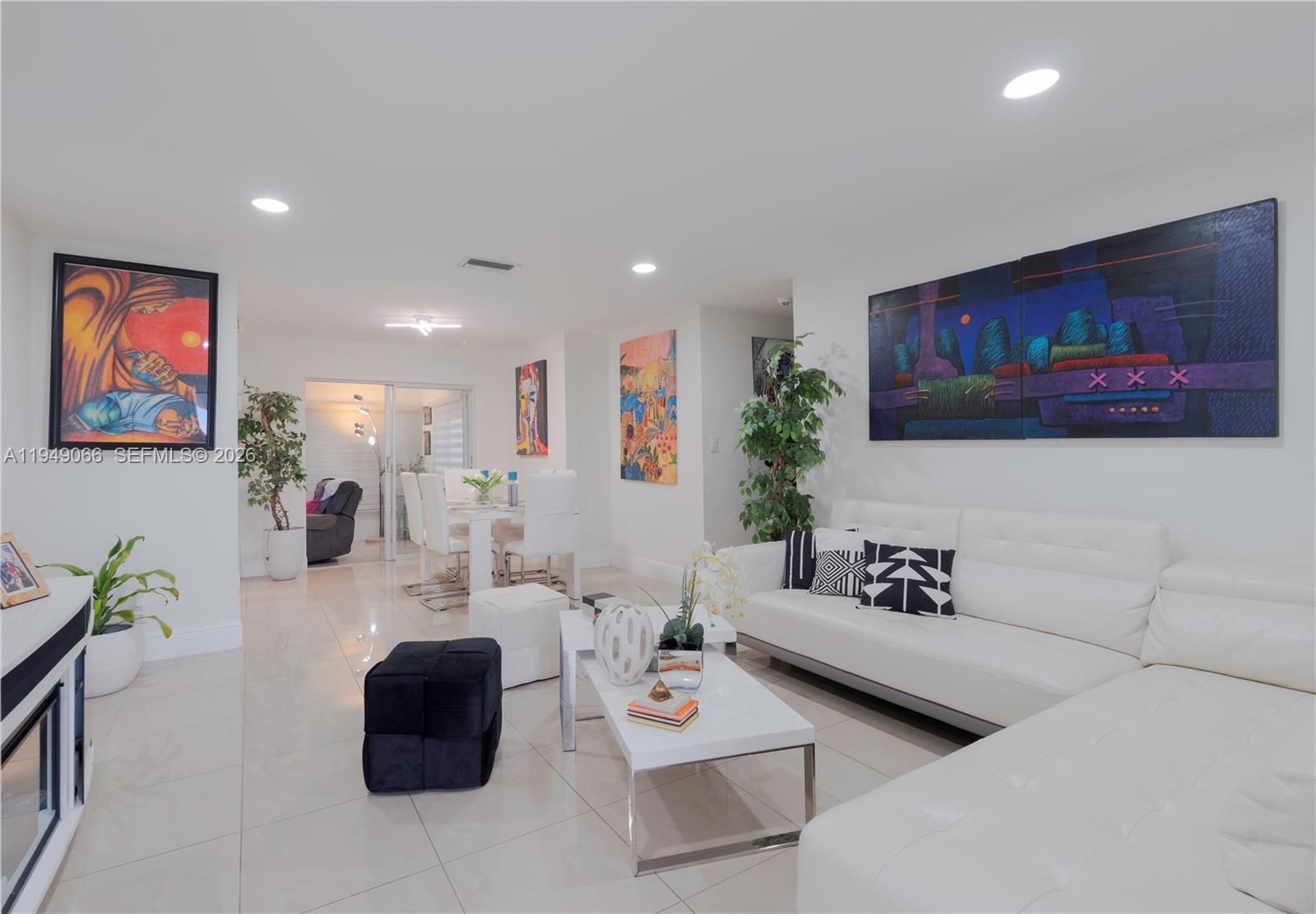 A modern living room features white tile floors, a white sectional sofa, and colorful artwork — 131 NW 31st Ct, Pompano Beach FL 33064, POMPANO BEACH, FL