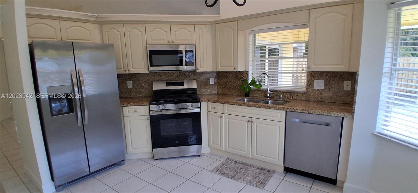 A kitchen features cream cabinets, granite countertops, stainless steel appliances, and white tile flooring — 3277 NW 123rd Ave, Sunrise FL 33323, SUNRISE, FL