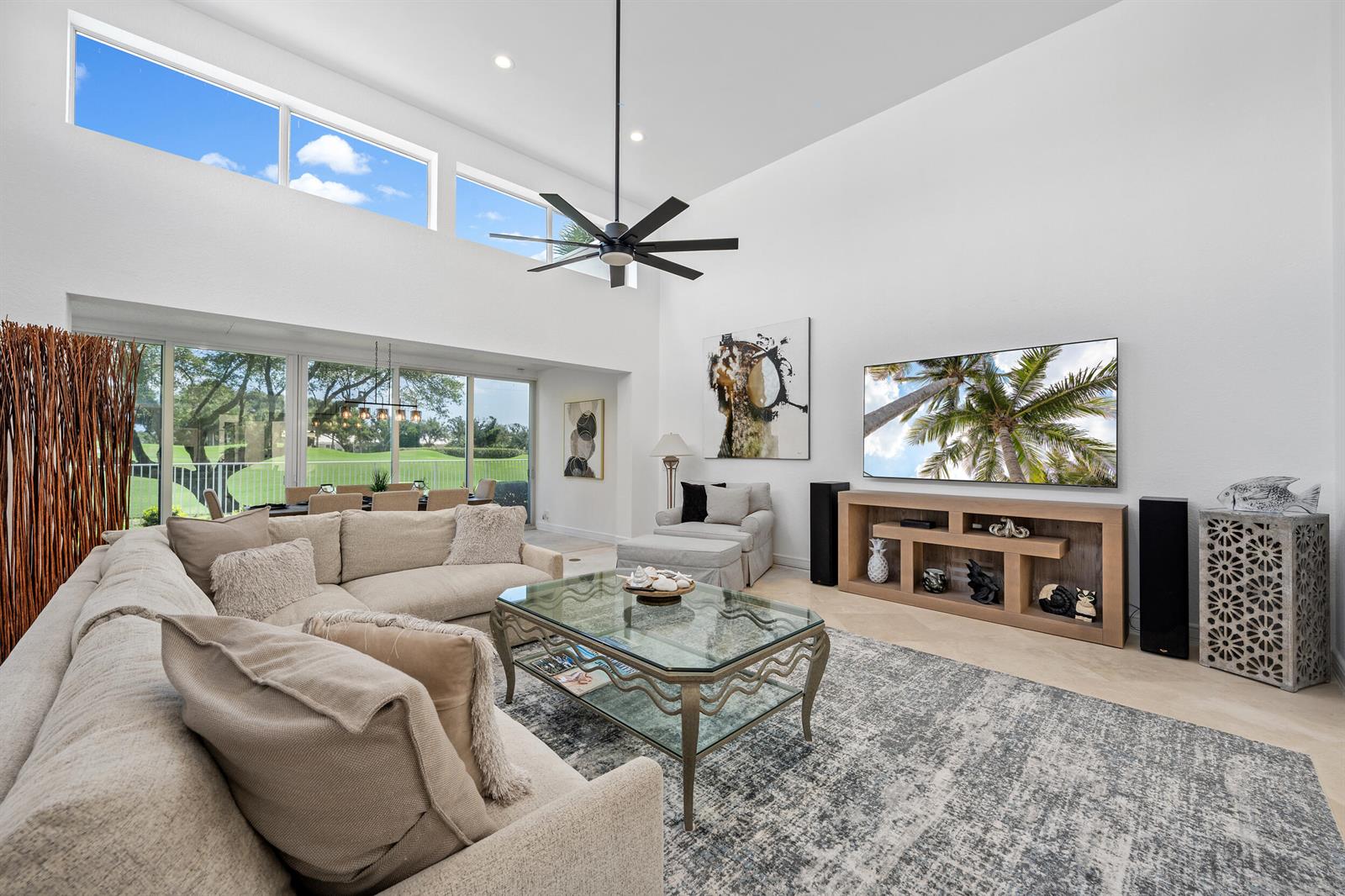 A spacious living room features high ceilings, large windows, a sectional sofa, and a television — 114 Waters Edge Drive, Jupiter FL 33477, JUPITER, FL