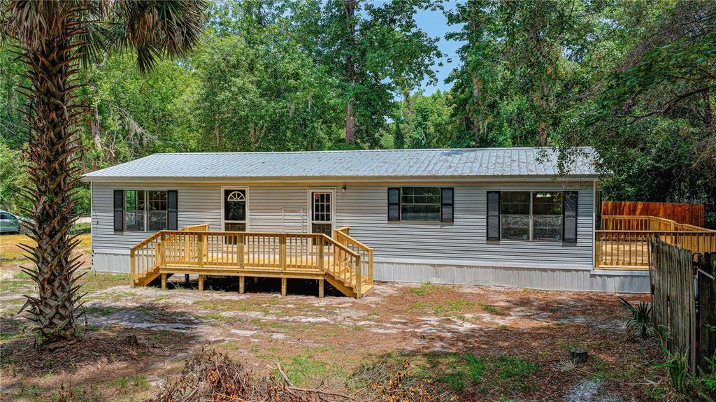 A single-story manufactured home with light gray siding, a metal roof, and wooden decks — 118 WATERWAY DRIVE, SATSUMA, FL