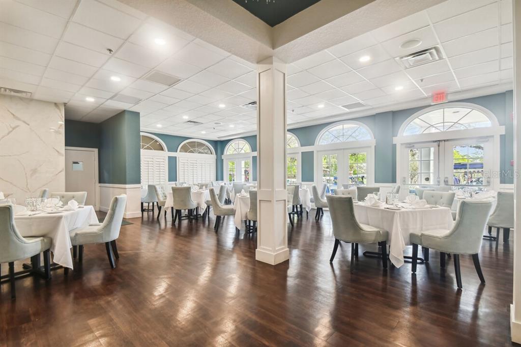 A dining room features white-clothed tables, upholstered chairs, dark wood flooring, and arched windows — 9104 WADE STREET UNIT Plan 2, WEEKI WACHEE, FL