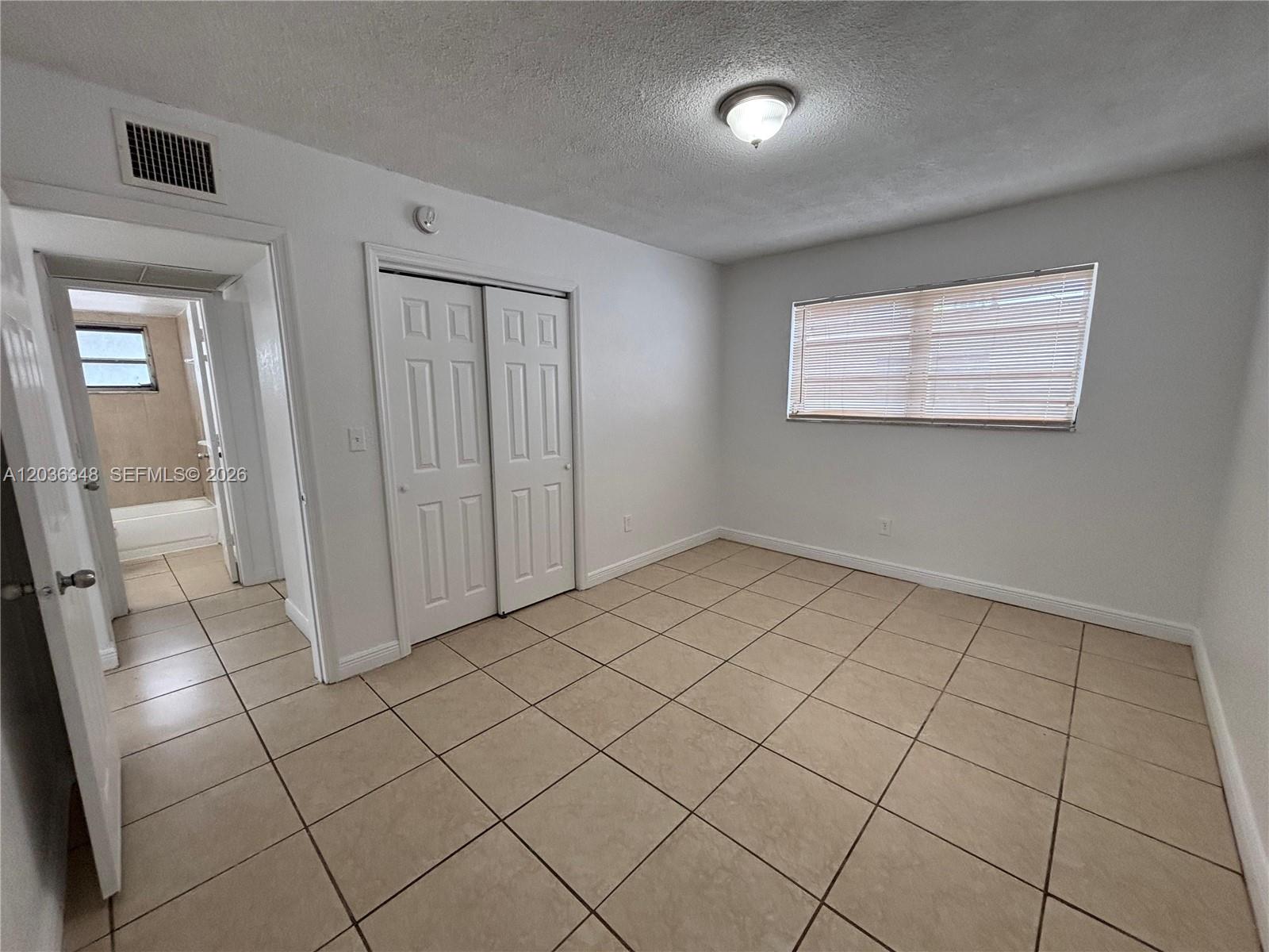 A bedroom with white walls, tile flooring, a sliding closet, and an attached bathroom — 8287 NE Miami Ct # 201, Miami FL 33138, MIAMI, FL