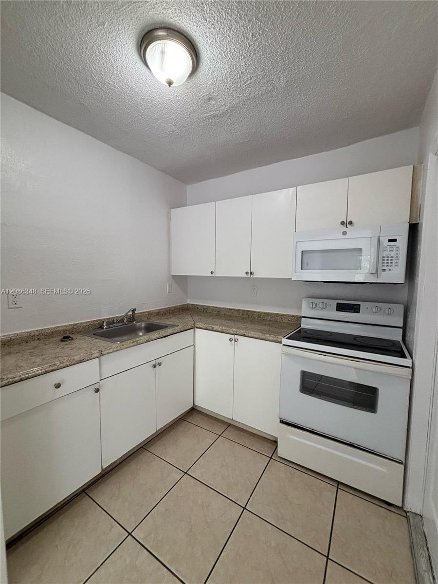 A small kitchen features white cabinets, a white stove, a microwave, and tan tile flooring — 8287 NE Miami Ct # 201, Miami FL 33138, MIAMI, FL