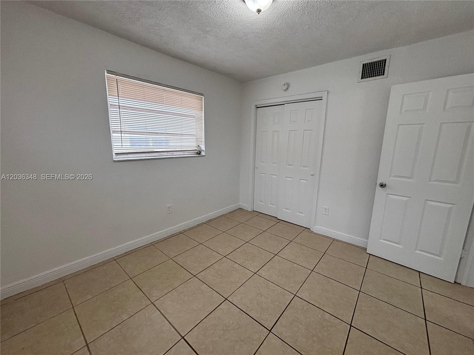 An empty bedroom features white walls, tan tile flooring, a window, and two white doors — 8287 NE Miami Ct # 201, Miami FL 33138, MIAMI, FL